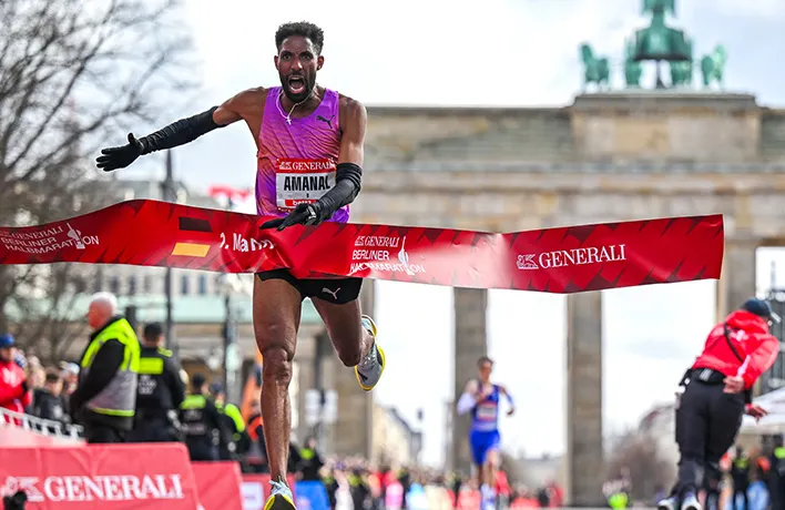 Die Ziel-Gerade des Berlin Generali Halbmarathon am Brandenburger Tor. Ein Läufer rennt durch das Zielbanner.