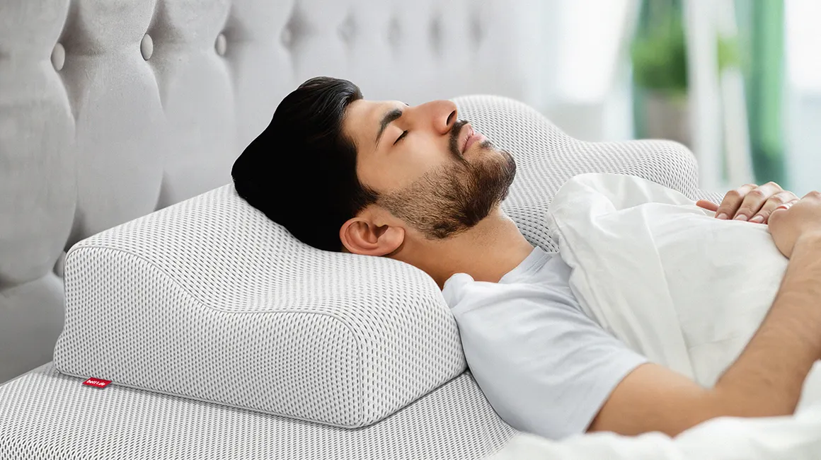  Photo: A person lies covered with their eyes closed in a bed on a BODYGUARD neck support pillow and the BODYGUARD mattress.