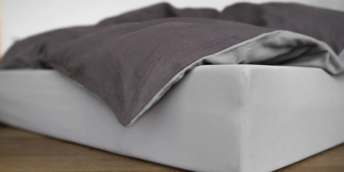 A mattress on the floor, with bedding in two-tone bed linen on top