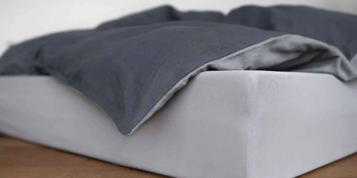 A mattress on the floor, with bedding in two-tone bed linen on top