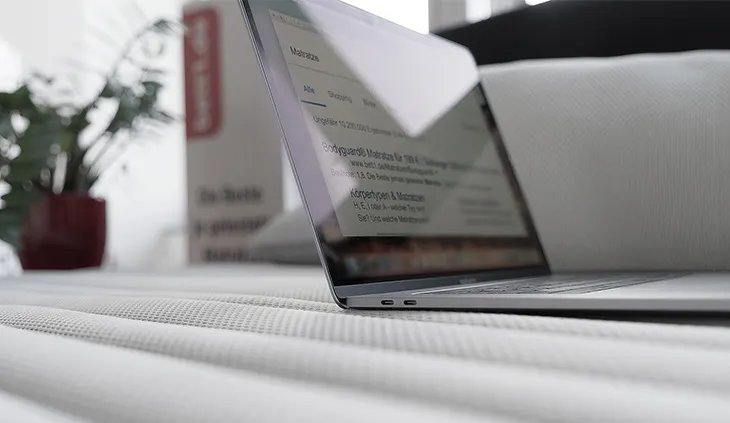 Ein Laptop steht aufgeklappt auf einer Matratze. Im Hintergrund steht der Karton einer BODYGUARD Matratze.