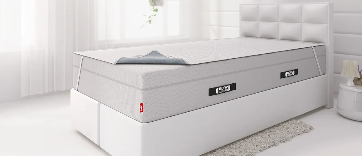 A box spring bed with an incontinence sheet stretched over the high mattress.