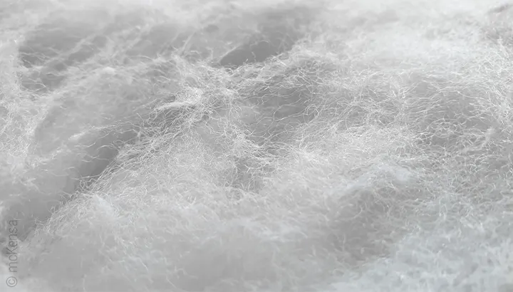 The image shows a close-up of fine white polyester fibres. The loose, voluminous fibre filling appears soft and fluffy.