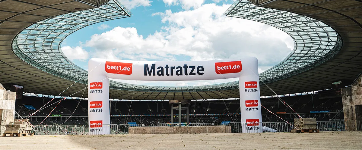 Inmitten des Olympiastadion Berlin steht ein großer luftbefüllter Bogen mit der Aufschrift: bett.de Matratze.