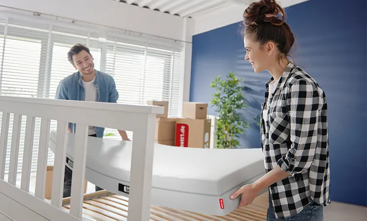 Two people lift a BODYGUARD Mattress into a bed frame