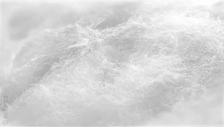 Close-up of fine, white polyester fibres. The loose, voluminous fibre filling looks soft and fluffy.