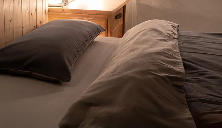 Photo: Reddish sunlight shines into a dark bedroom onto a bed covered with flannel winter bedding.