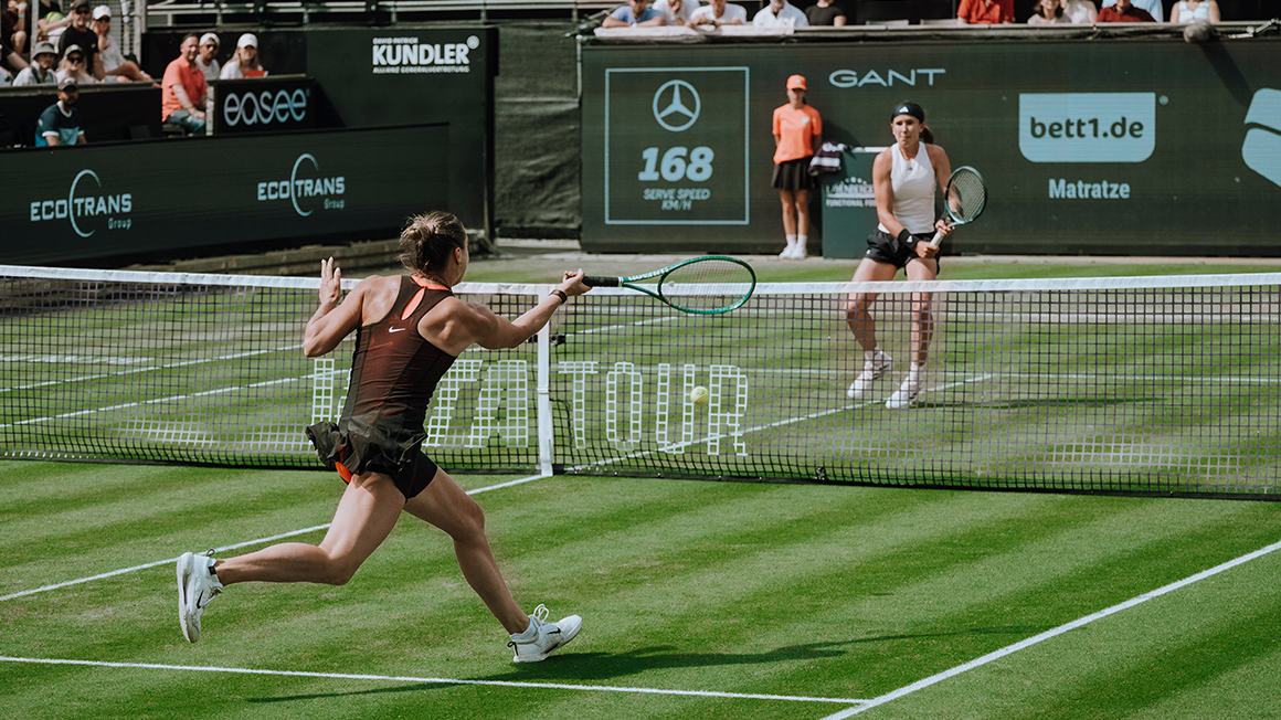 Two women are playing tennis on a grass court.