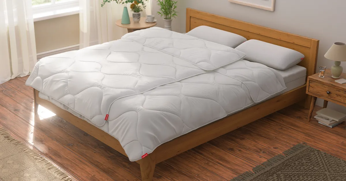 Ein helles, modern eingerichtetes Schlafzimmer mit Doppelbett. Darauf liegen ordentlich ausgebreitet zwei BODYGUARD Bettdecken 135x200 cm sowie zwei Kissen.