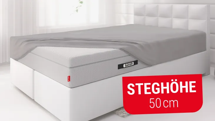 Foto: Schlafzimmer mit Bett. Darauf liegt die BODYGUARD Boxspring-Matratze, halb bezogen mit BODYGUARD Spannbettlaken 100x200 cm extra hoch. Text: Steghöhe 50 cm