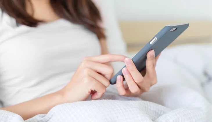 Eine Person liegt mit Smartphone in der Hand im Bett und berührt das Display mit einem Finger.