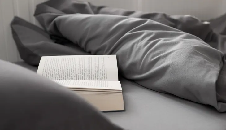 Photo: An open book lies on a sheet under a folded-back duvet.