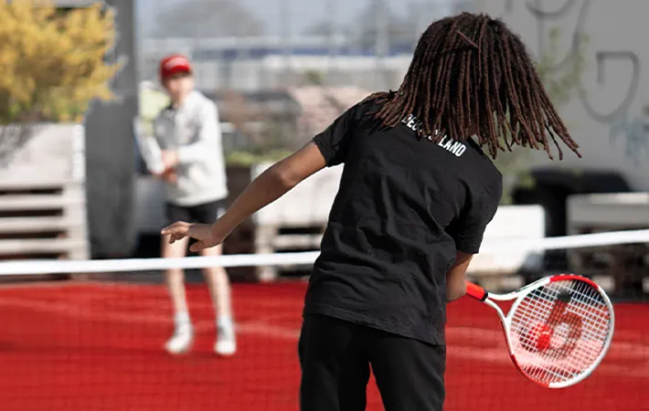 Foto: Ein Kind spielt einen Tennisball über ein Netz zu einem anderen Kind.