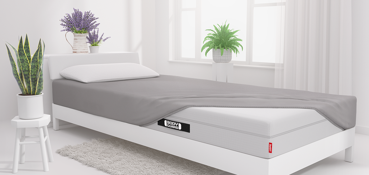 A mattress half-covered with a fitted sheet in a bright bedroom.