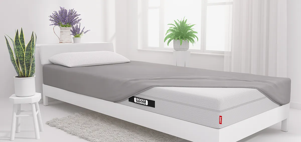 A mattress half-covered with a fitted sheet in a bright bedroom.