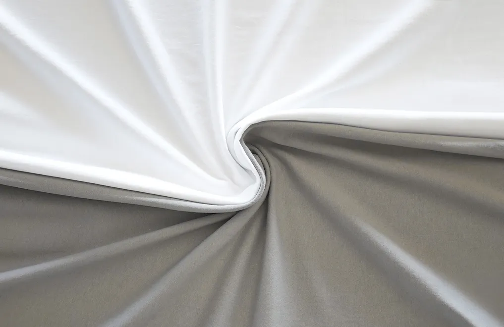 Photo: Two BODYGUARD jersey fitted sheets, one in silver and the other in white. The sheets are lying side by side and have been twisted together in the middle.