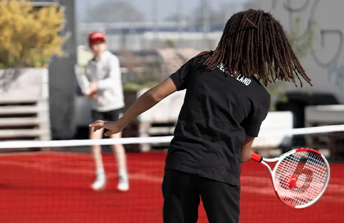 Foto: Ein Kind spielt einen Tennisball über ein Netz zu einem anderen Kind.