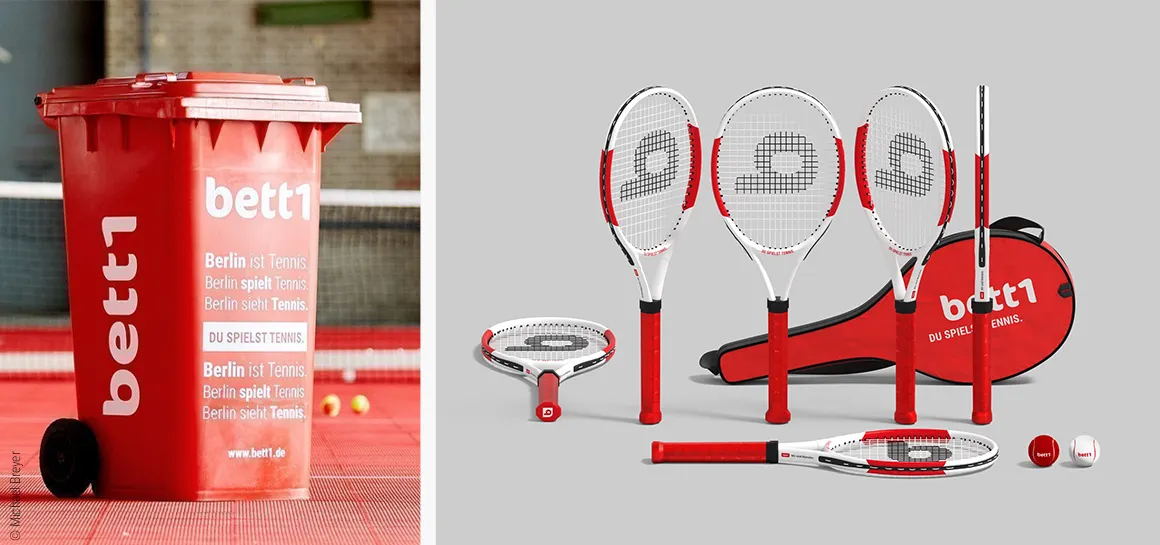 Foto: Links eine rote Tonne mit der Aufschrift „bett1.de – Tennis macht Schule“; rechts mehrere Tennisschläger, eine Schlägertasche mit der Aufschrift „bett1.de – Du spielst Tennis“ und zwei Tennisbälle.