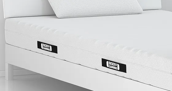 The BODYGUARD mattress 100x220 cm lies on a simple wooden bed, accompanied by a pillow.