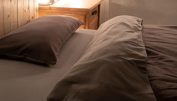 Photo: In a warmly lit bedroom, pillows and blankets covered with flannel winter bed linen lie on the bed. The duvet is folded back slightly so that the dark and light sides of the flannel bed linen are visible.