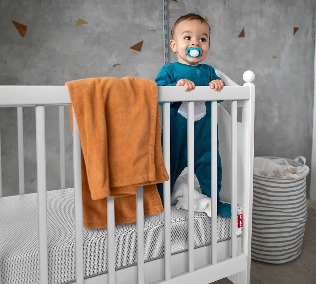 Baby steht in Gitterbett auf der SuperBreeze Kindermatratze