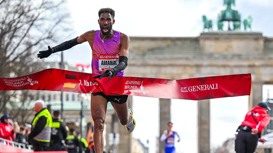 Die Ziel-Gerade des Berlin Generali Halbmarathon am Brandenburger Tor. Ein Läufer rennt durch das Zielbanner.