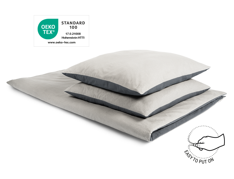 The BODYGUARD® Flannel Bed Linen covered on a folded duvet with two pillows. The Oeko-Tex® seal. Illustration of a hand closing a zip. Text: easy to cover	