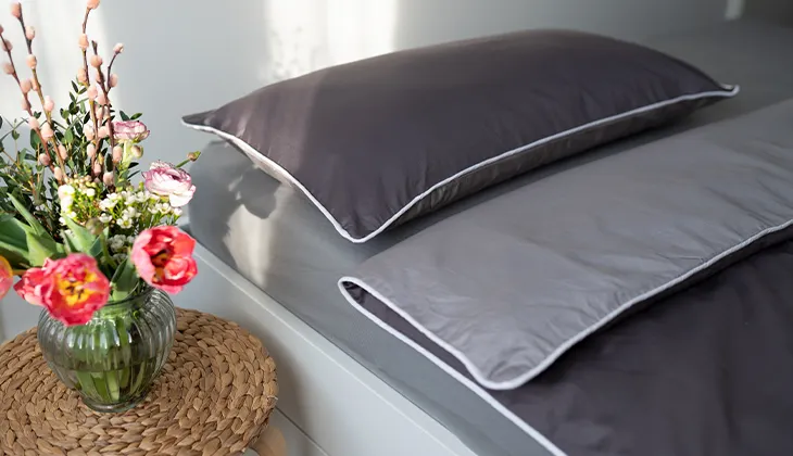 Photo: A made bed covered with summer bed linen made of satin, with a colourful bouquet of flowers on the bedside table.