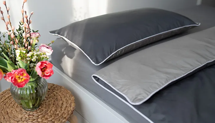 Photo: A made bed covered with summer bed linen made of satin, with a colourful bouquet of flowers on the bedside table.