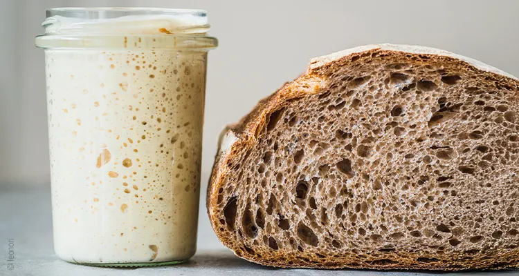 Photo: A glass of sourdough stands next to a loaf of sliced bread. Gas bubbles and pores are visible in both.
