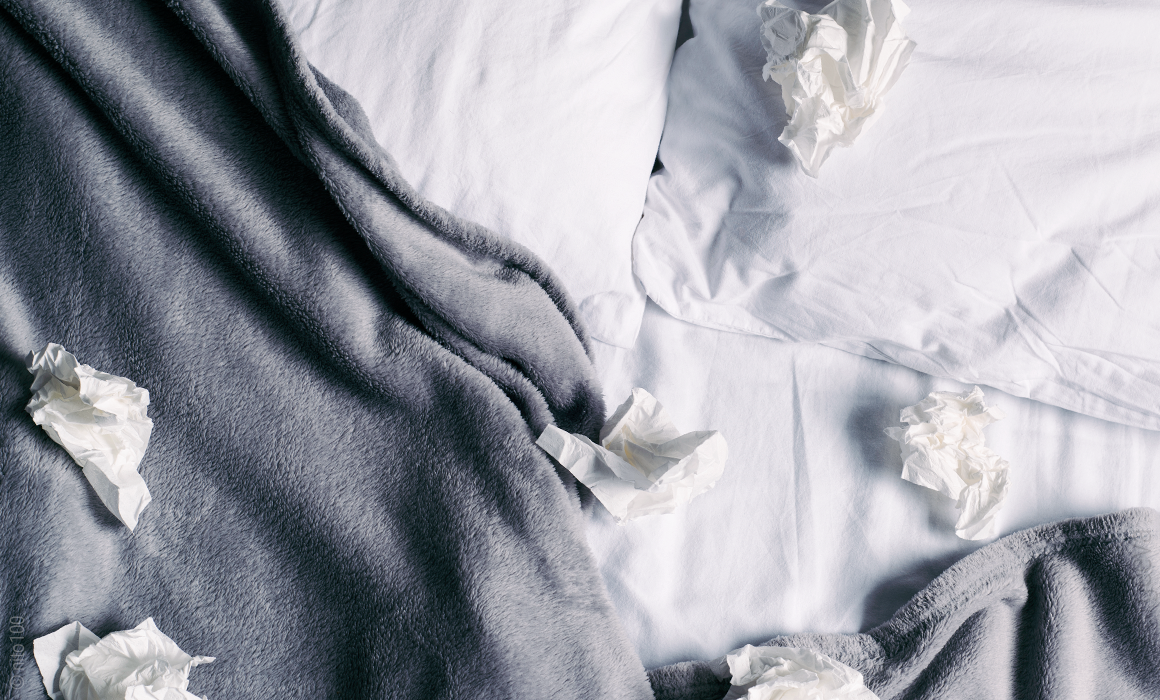 There are a few used tissues lying on a rumpled bed.