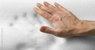 A hand hovers over a foam mattress made of visco foam in which the handprint is still visible