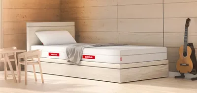 Die BODYGUARD Anti-Kartell-Matratze Weich in einem hellen Zimmer. Die Wände sind mit hellem Holz vertäfelt. Rechts neben dem Bett steht eine Gitarre.