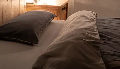 Foto: Rötliches Sonnenlicht scheint in ein dunkles Schlafzimmer auf ein mit Winterbettwäsche aus Flanell bezogenes Bett.