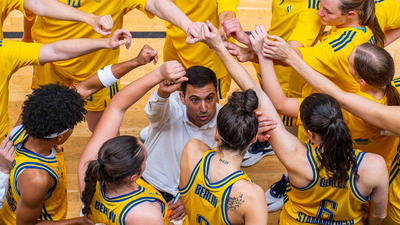 Photo from a bird's eye view: A person in a white shirt surrounded by people in yellow jerseys who put their hands over each other in the middle.