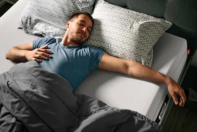 Foto: Eine Person liegt mit geschlossenen Augen auf einer BODYGUARD Matratze in einem nächtlichen Schlafzimmer.