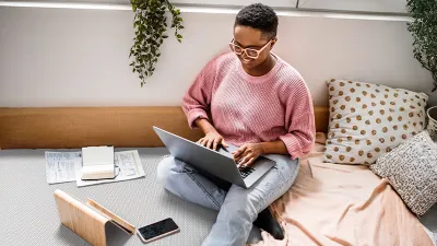 A person is sitting on the floor with an open laptop on their legs. 