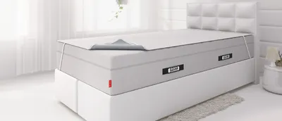 Ein Boxspringbett, auf dessen hoher Matratze eine Inkontinenzauflage gespannt ist.