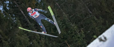 Photo: A person with skis in a jumping pose above a snowy forest.