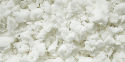 Close-up of white memory foam flakes with a soft, fluffy texture. The irregularly shaped foam pieces appear light and airy and are densely packed together.