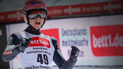 Photo: A person in a jersey, with ski goggles and helmet, holds his arms bent in front of his body and has his mouth wide open.