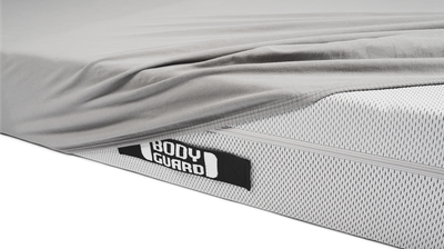 The BODYGUARD jersey fitted sheet lies half-unfolded on a bett1 mattress