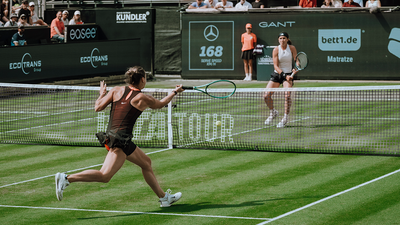 Two women are playing tennis on a grass court.