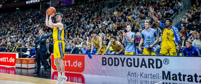 Photo: Game scene in a dark hall. Players in blue and yellow jerseys, one person throws the ball towards the basket.