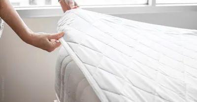 Foto: Zwei Hände greifen einen Matratzenschoner, der auf einer Matratze liegt an einer Ecke