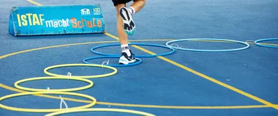 A parkour course made of hula hoops lies on a playing field and children’s legs are jumping through it; behind it is a banner with the text: ISTAF sets the standard.