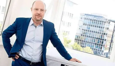 bett1-Gründer Adam Szpyt lehnt an einer BODYGUARD Matratze. Im Hintergrund steht ein Gebäude mit vielen Fenstern.