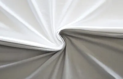 Photo: Two BODYGUARD jersey fitted sheets, one in silver and the other in white. The sheets are lying side by side and have been twisted together in the middle.