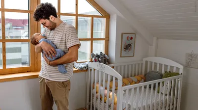 Photo: A person standing next to a crib, holding a baby in their arms.