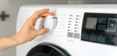 Photo: The control panel of a washing machine. A hand reaches for a control knob.